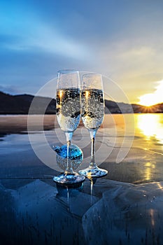 Champagne glasses stand on the ice of the frozen Lake Baikal. Christmas blue balloons and two glasses of champagne.