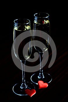 Champagne in glasses and two red hearts on a black background