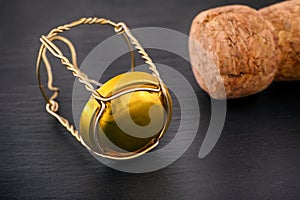Champagne muselet with gold cap and cork on black stone background
