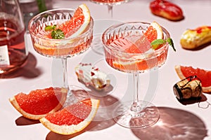 Champagne, rose sparkling wine or paloma cocktails in crystal glasses on pink background with mini eclairs. Refreshing