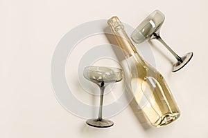 Champagne or sparkling wine bottle, champagne glasses from tinted grey glass on beige background. Festive drink minimal