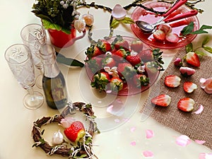 Champagne and  two glass with sweet strawberries and slices on a white background, flowers in a red cup and  branch in the shape o