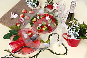 Champagne and  two glass with sweet strawberries and slices on a white background, flowers in a red cup and  branch in the shape o