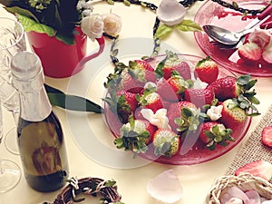 Champagne and  two glass with sweet strawberries and slices on a white background, flowers in a red cup and  branch in the shape o