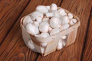 Champignon mushrooms in a basket on a wooden table.