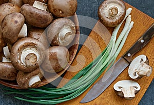 Champignon mushrooms in a wooden bowl and green onions, close-up, top view