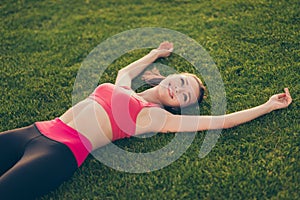 Champion. Well done! Exhausted cheerful sportive woman is relaxing after a fitness workout, lying on the green grass in a spring