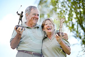 Champions of golf. Low angle view of a mature couple laughing and smiling with their golfing trophies.