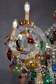 The chandelier is gold in color, with light bulbs in the form of a candle. Crystal pendants, colored glass pendants