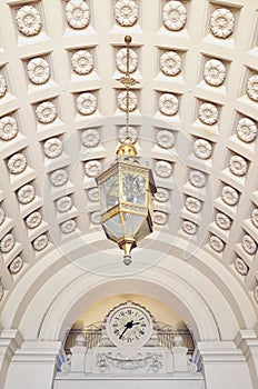 Chandelier Hanging from Ornamented Ceiling in front of a Clock