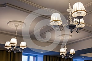 Chandeliers with three electric lamps and lampshades hanging on