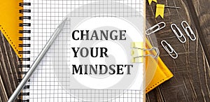 CHANGE YOUR MINDSET text on a sticker on the notebook, wooden background