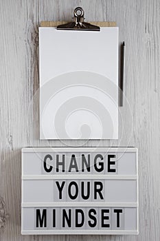 `Change your mindset` words on a modern board, clipboard with blank sheet of paper on a white wooden surface. Top view, from abo