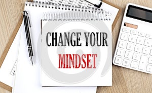 CHANGE YOUR MINDSET is written in white notepad near a calculator, clipboard and pen. Business concept