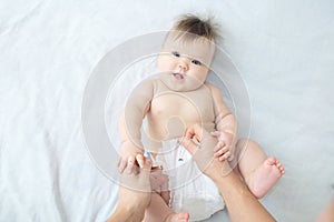 Changing diaper on baby girl on bed, changing nappy, smiling baby portrait