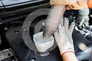 Changing the engine oil. A car mechanic pours oil from a bottle through a funnel into the engine filler neck
