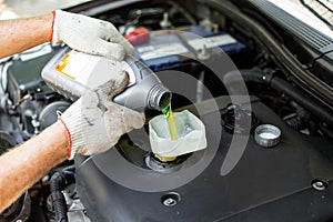 Changing the engine oil. A car mechanic pours oil from a bottle through a funnel into the engine filler neck