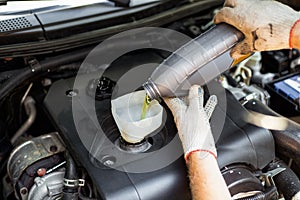 Changing the engine oil. A car mechanic pours oil from a bottle through a funnel into the engine filler neck