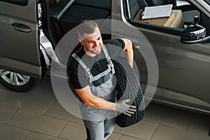 Changing tires season. Man in uniform is working in the autosalon at daytime