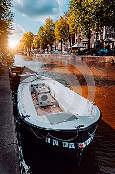 Channel in Amsterdam at autumn sunset. Boat in front of tree-lined canal, white clouds in the sky. Netherlands houses landmark