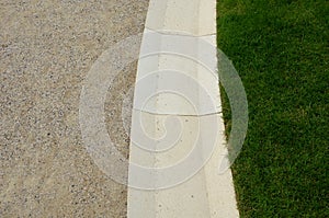Channel for drainage of water from a gravel road made of beige sandstone stone purely worked stoneware connects to a short mown