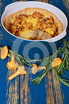 Chanterelle mushroom pie with cheese and herbs in the baking dish decorated with fresh rosemary on the wooden rustic kitchen table