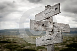 Chaos, Confusion and doubt text on wooden signpost outdoors in the wilderness.