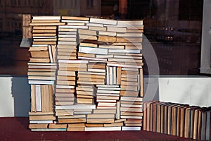 Chaotic pile of books lies in disorder on bookstore window, acoffee shop or library.