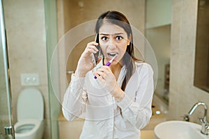 Chaotic preparation for work in the morning.Young woman talking on the phone while brushing teeth and putting on clothes.Busy