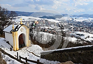 Kaple banskoštiavnické kalvárie u horního kostela v zimní sezóně se zasněženým schodištěm a částí panoráma města v pozadí