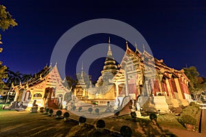 Chapel and golden pagoda at Wat Phra Singh Woramahawihan in Chiang Mai at twilight or night with stars in sky