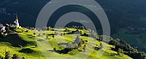 Chapel and sheep on the meadow. Bell tower, trees, shrubs and hilly green grassland. Heiliger Antoniuse church and houses