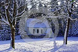 Chapel in snowy forest landscape with snowman at path