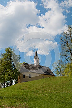 Chapel St Georg and trees at Weinberg hill, spring landscape Schliersee. blue sky with clouds