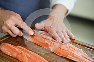 Char fish filleting, hands of the cook remove the bones with a thin fillet knife on a cutting board, selected focus