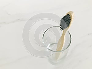 Charcoal infused bamboo toothbrush in glass with marble white background. Top view.