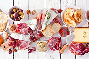 Charcuterie board of assorted cheeses, meats and appetizers, above view table scene over white wood