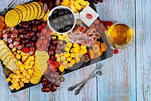 Charcuterie board with cheese, olives, fruits, prosciutto and wine on wooden table