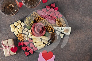 Charcuterie board for Valentines Day with varieties sausage, cheese, nuts, olives and two glass rose wine on brown