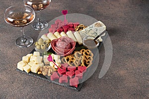 Charcuterie board for Valentines Day with varieties sausage, cheese, nuts, olives and two glass rose wine on brown