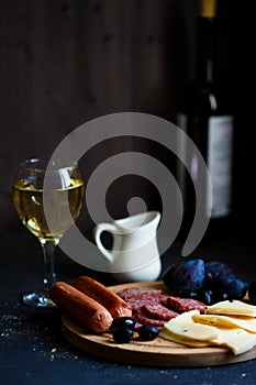 Charcuterie, grilled sausages, cheese, salami, plum olives and a glass of wine on a dark table