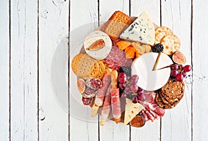 Charcuterie platter with different meats, cheeses and appetizers over a white wood photo