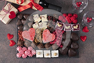 Charcuterie sweet board with different sweets, chocolate, marmalade hearts, nuts and candies as well wine and two glass