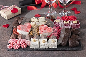 Charcuterie sweet board with different sweets, chocolate, marmalade hearts, nuts and candies as well wine and two glass