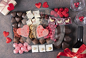 Charcuterie sweet board with different sweets, chocolate, marmalade hearts, nuts and candies as well wine and two glass