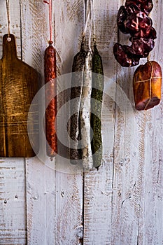 Charcuterie, variety of sausages hanging on hook, wood cutting board, string with dry peppers nyora, Spanish meat delicacies photo