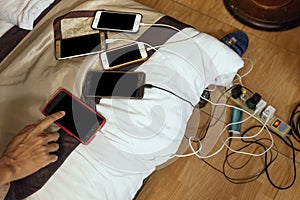 Charged smart phones with right hand pointed on bed with charge cords in a mess at hotel room in Hanoi, Vietnam