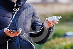 Charger in the female hand of a tourist with a discharged smartphone lifestyle outdoors. Selective focus on charging