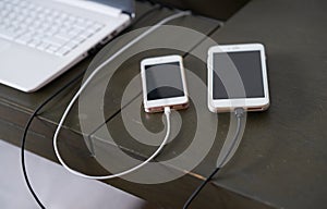 Charger line of two smart phone on wooden table surface for energy consumption on wooden table