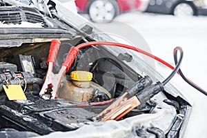 Charging automobile discharged battery by booster jumper cables at winter photo